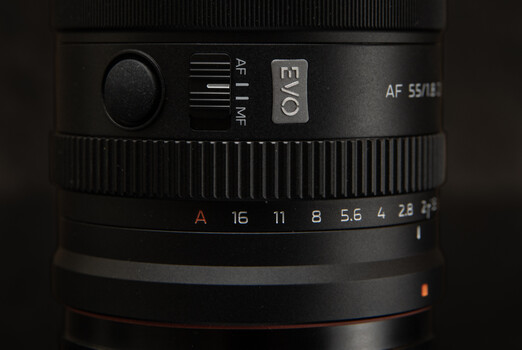 Close-up of camera lens showing aperture ring with f-stop markings from f/16 to f/2.8 and autofocus controls.
