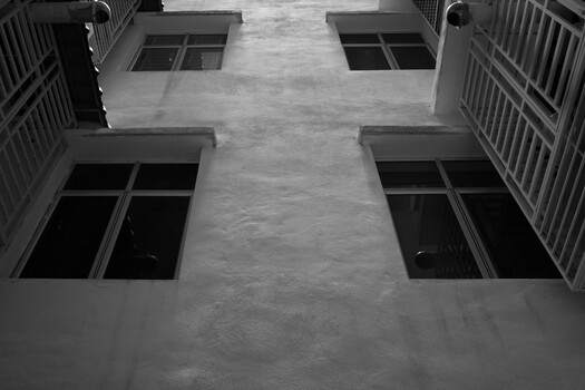 Upward view of a concrete courtyard framed by four residential buildings with barred windows and metal railings.