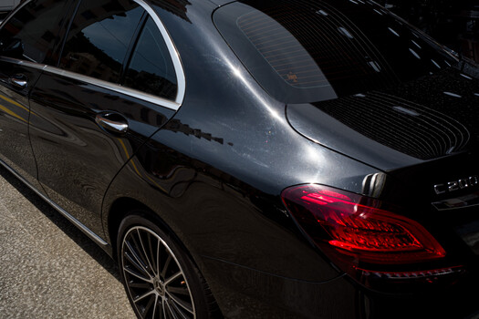 Black luxury sedan photographed from the rear three-quarter angle, highlighting the taillight and body line detail in daylight.