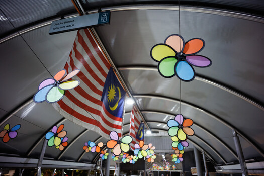 Colorful flower decorations and a Malaysian flag hanging inside a modern transit vehicle.