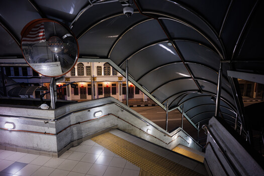 Modern subway station platform with curved architectural canopy and warm-lit building facade at night.