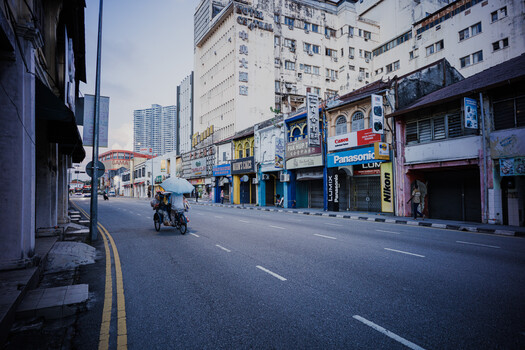 Early morning urban street with storefronts, motorcyclist, and high-rise buildings under overcast sky.
