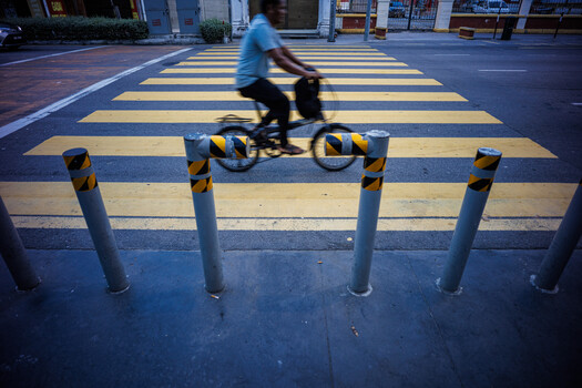 Cyclist riding through a zebra crossing with yellow and black bollards in the foreground.