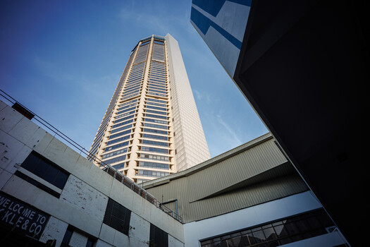Tall residential tower shot from below against clear blue sky, framed by lower concrete structures.