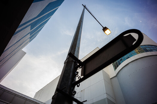 Low-angle view of modern glass and steel buildings with a black street lamp in the foreground against a blue sky.