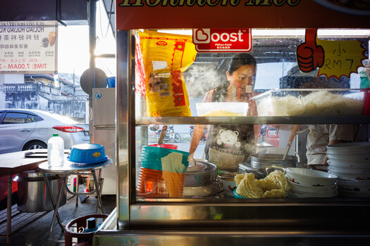 Street food vendor preparing food behind a glass counter in a storefront window.