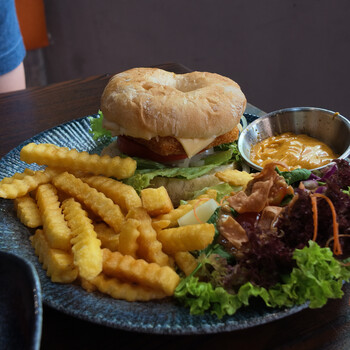 Burger with waffle fries and garnishes plated on a dark textured plate.
