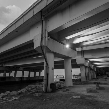 Concrete pillars supporting massive highway overpasses shot from below in black and white.