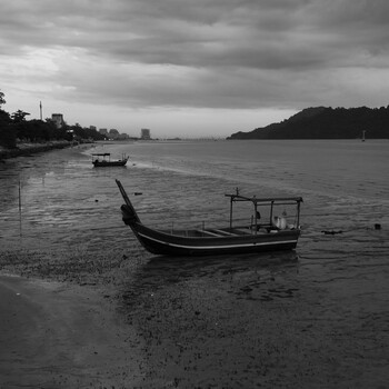Traditional wooden boats moored in shallow water under dramatic cloudy sky.