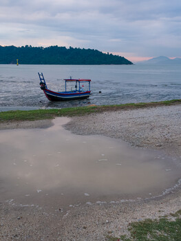 Wooden fishing boat moored in shallow water near a sandy beach at dusk.