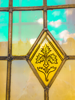 Yellow diamond-shaped stained glass panel with ornamental floral design set in lead came framework.