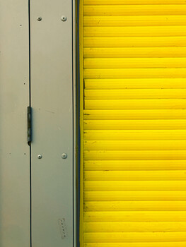 Minimalist composition of a beige metal door and bright yellow corrugated metal wall.