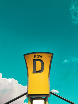 Bright yellow stadium seating sign reading 'ROW D' against a turquoise sky with white clouds.