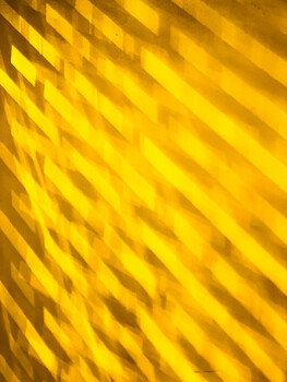 Diagonal stripes of yellow and gold light creating a layered shadow pattern on a textured surface.
