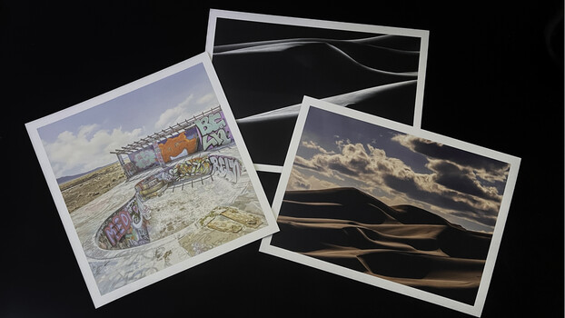 Three printed photographs arranged on a black surface, displaying landscape and architectural imagery with varied tonal ranges.