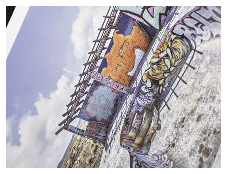 Tilted aerial view of colorful street murals and graffiti art on urban walls beneath blue sky.