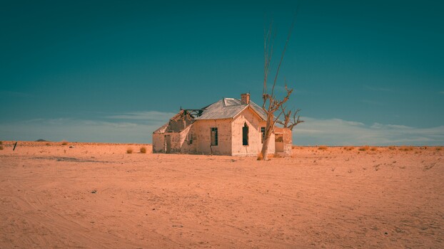 Abandoned adobe house in vast desert landscape with clear blue sky.