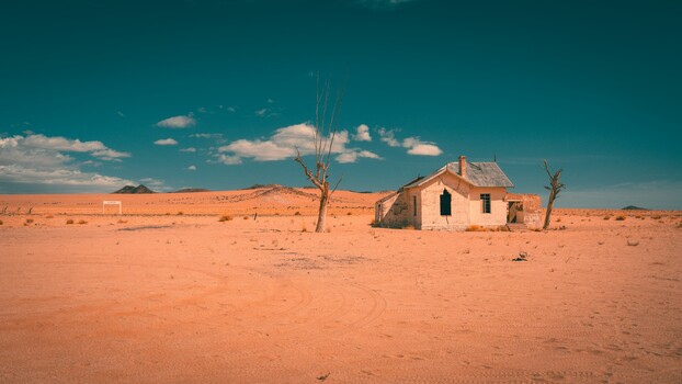 Abandoned brick house standing alone in vast desert landscape under clear blue sky.