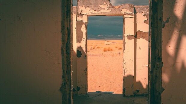 Weathered green doorframe opening onto an arid desert landscape with sparse vegetation and blue sky.