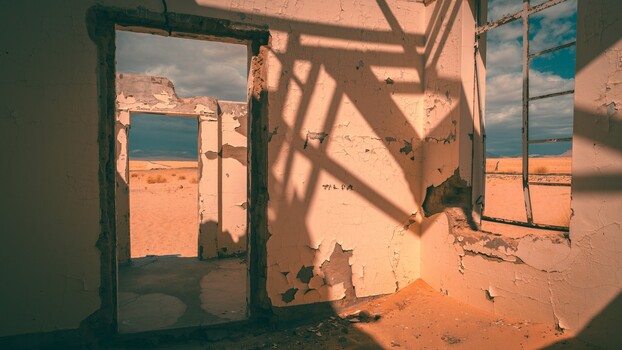 Abandoned building interior with open doorways framing desert landscape and sky beyond.