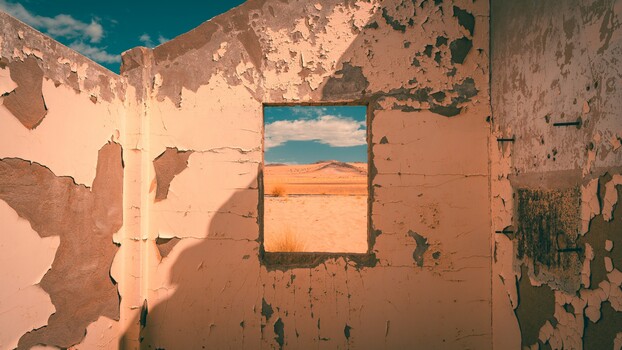 Abandoned building interior with peeling terracotta walls framing a desert landscape view through a window opening.
