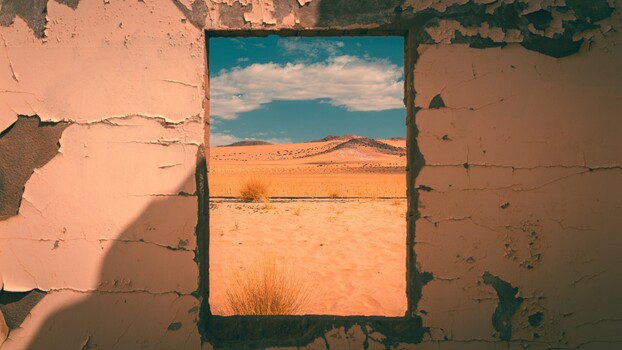 Desert landscape framed by a weathered window opening in a crumbling clay wall.