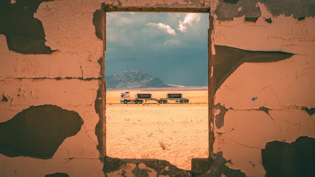 Trucks and desert landscape framed through a decaying brick doorway.