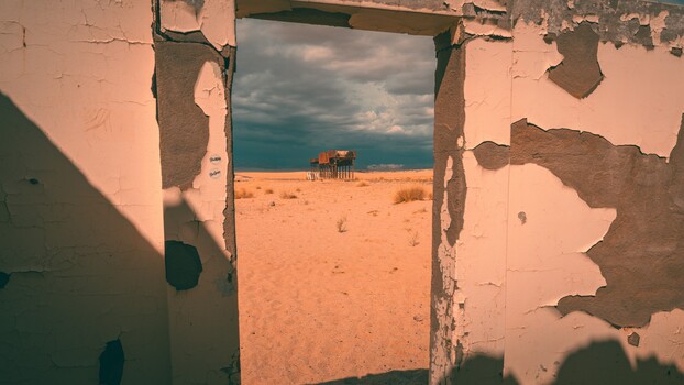 Framed view through deteriorating doorway to beach structure and ocean horizon.