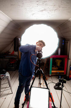 Photographer adjusting a camera on a tripod inside a large circular light modifier.