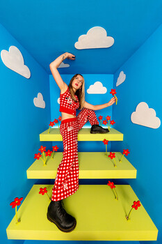 Illustration of a woman in red polka-dot clothing posing dynamically on stacked yellow platforms against a blue sky with white clouds.