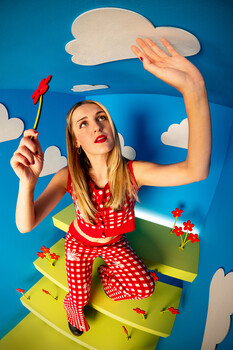 Woman in red polka-dot outfit reaching toward white paper cloud cutout against blue background with yellow platform and clouds.
