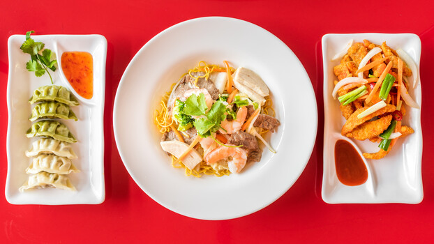 Three white rectangular and one round white plate with Asian cuisine arranged symmetrically on bright red background