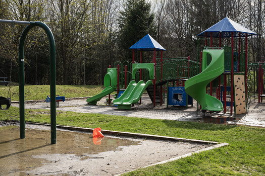 Wet playground with green slides and colorful equipment surrounded by leafless trees