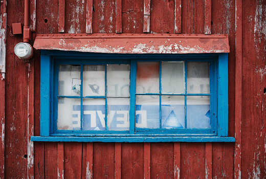 Bright blue-framed window with white panes set into weathered red wooden wall