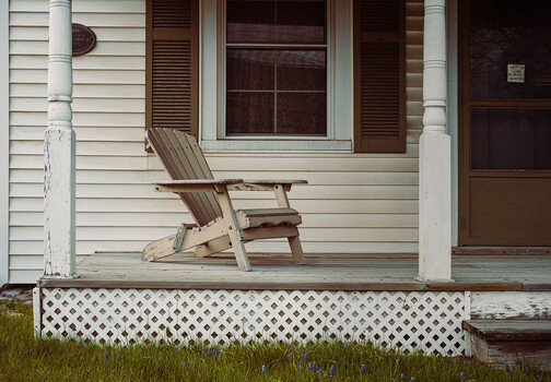 Wooden Adirondack chair on a covered porch with white railings and columns