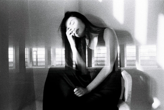 Woman with long dark hair in contemplative pose, hand to face, shot in high-contrast black and white