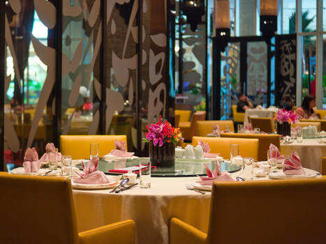 Fine dining restaurant interior with yellow banquette seating, white tablecloths, and pink floral centerpieces