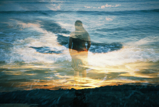 Double exposure portrait merging silhouetted figure with ocean waves and sunset landscape