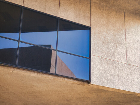 Modern architectural facade with large windows reflecting blue sky and adjacent building