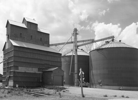Black and white photograph of industrial grain elevator complex with wooden tower and metal storage silos