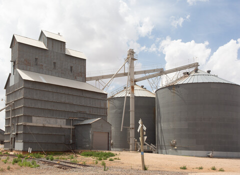 Weathered grain elevator and storage silos under partly cloudy sky