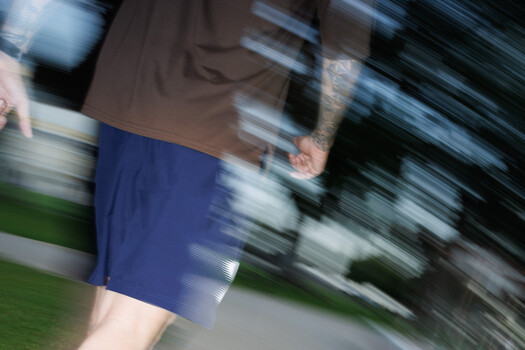 Motion-blurred runner in blue shorts captured with panning technique during outdoor exercise