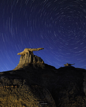 Desert rock formation silhouetted against star trail night sky