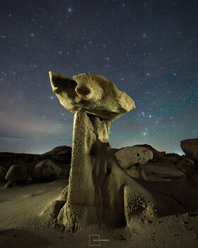 Tall rock formation illuminated by light against starry night sky in desert landscape