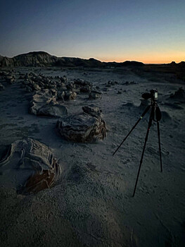 Tripod-mounted camera on rocky desert landscape at twilight