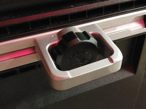 White tray holding black camera lens cap inside large-format printer with pink LED accent lighting