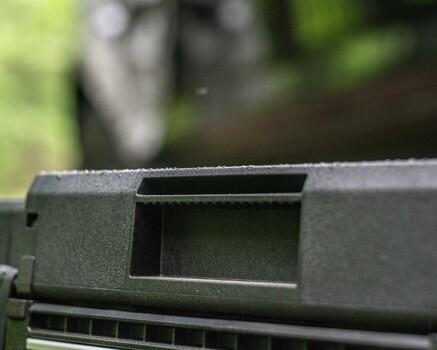 Close-up of a rifle's ejection port and charging handle against a blurred outdoor background