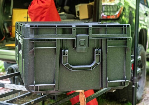 Olive green hard case with dual handles and metal reinforcement on workshop table