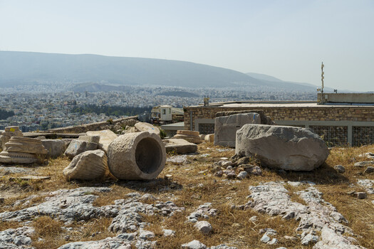 Abandoned stone architectural elements and rubble on hillside overlooking dense cityscape