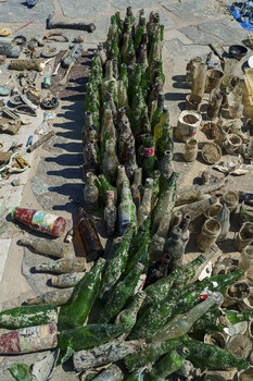 Tall green cactus surrounded by discarded metal debris and rocks on sandy ground